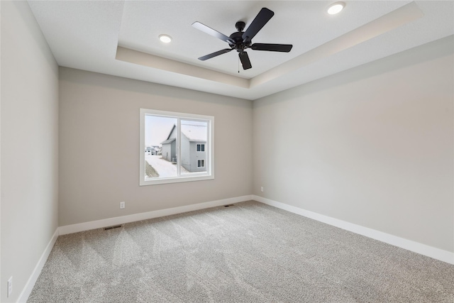 carpeted spare room featuring a tray ceiling and ceiling fan