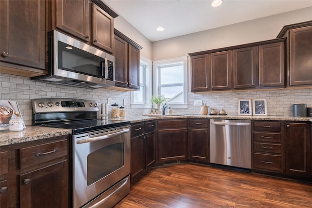 kitchen with dark brown cabinets, light stone counters, dark hardwood / wood-style floors, stainless steel appliances, and backsplash