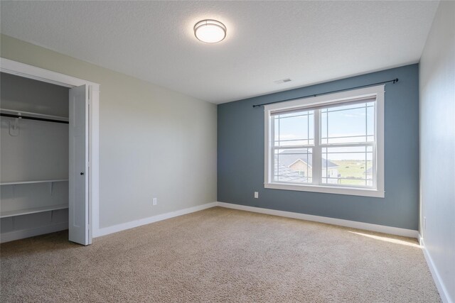 unfurnished bedroom with light carpet, a textured ceiling, and a closet