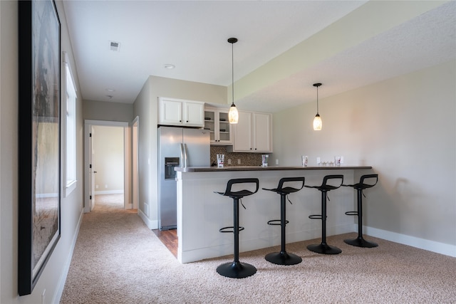 kitchen with stainless steel fridge, white cabinets, kitchen peninsula, a breakfast bar area, and carpet flooring