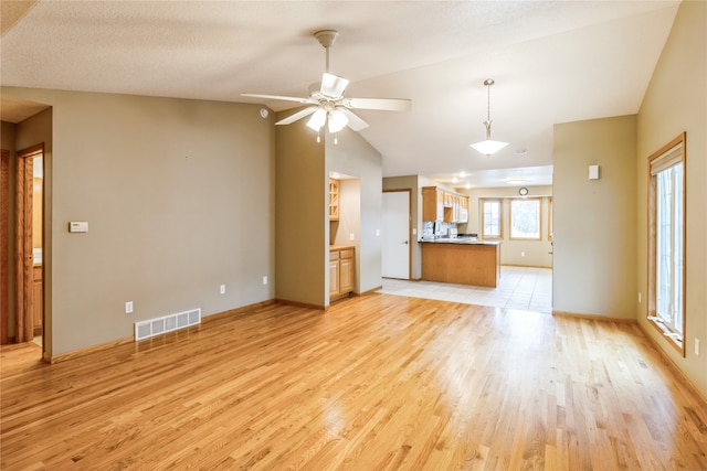 unfurnished living room with light hardwood / wood-style flooring, vaulted ceiling, ceiling fan, and a textured ceiling