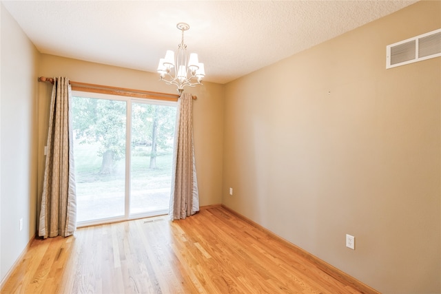 spare room with a textured ceiling, an inviting chandelier, and light hardwood / wood-style flooring