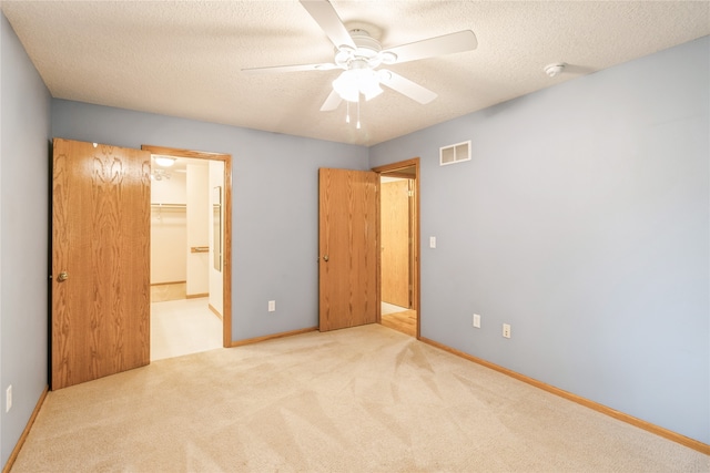 unfurnished bedroom featuring a spacious closet, a closet, light colored carpet, and ceiling fan