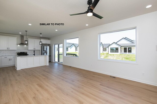 kitchen featuring stainless steel appliances, hanging light fixtures, wall chimney range hood, light hardwood / wood-style floors, and white cabinets