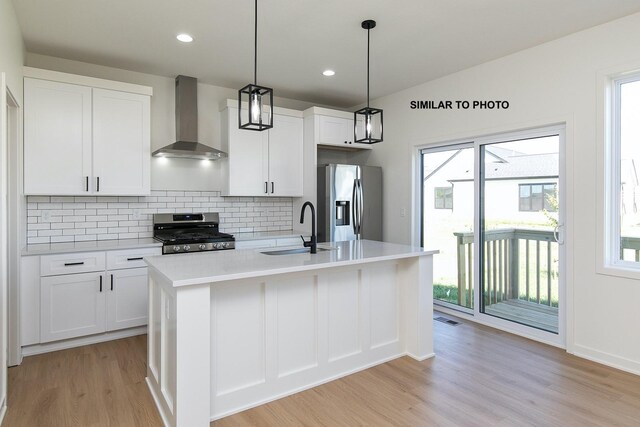 kitchen featuring a kitchen island with sink, sink, wall chimney exhaust hood, and appliances with stainless steel finishes