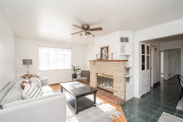 living room featuring ceiling fan, a stone fireplace, and a textured ceiling