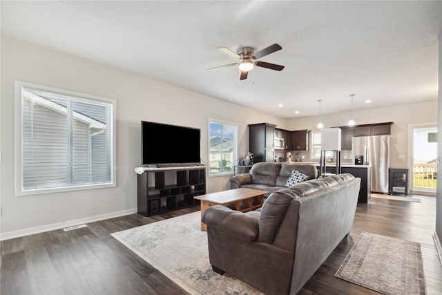 living room featuring a wealth of natural light, ceiling fan, and dark wood-type flooring