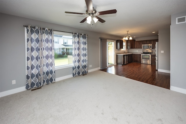 unfurnished living room featuring a healthy amount of sunlight, ceiling fan with notable chandelier, and dark wood-type flooring