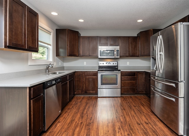 kitchen with appliances with stainless steel finishes, dark wood-type flooring, a textured ceiling, dark brown cabinets, and sink