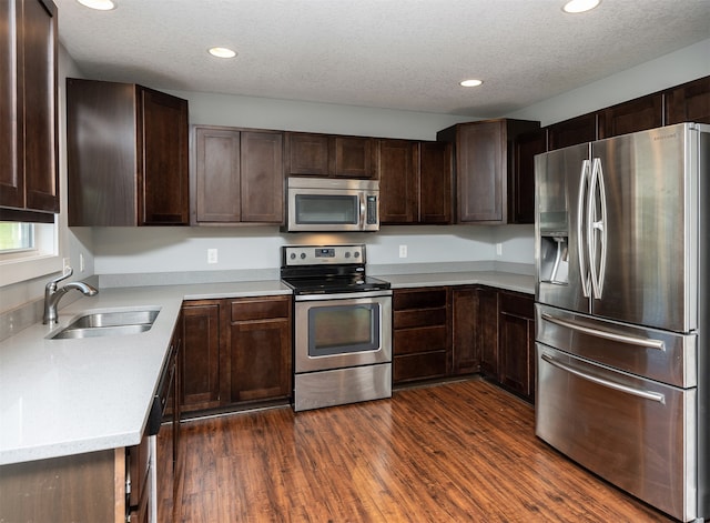 kitchen with appliances with stainless steel finishes, a textured ceiling, dark brown cabinets, dark hardwood / wood-style floors, and sink