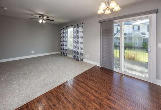 empty room featuring ceiling fan with notable chandelier, dark hardwood / wood-style floors, and plenty of natural light