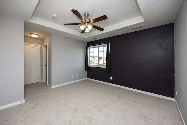 carpeted spare room with a textured ceiling, a raised ceiling, and ceiling fan