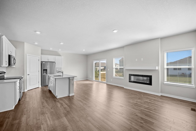 kitchen with appliances with stainless steel finishes, white cabinetry, wood-type flooring, a kitchen island with sink, and sink