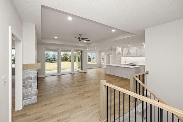 living room featuring a raised ceiling, ceiling fan, sink, and light hardwood / wood-style floors