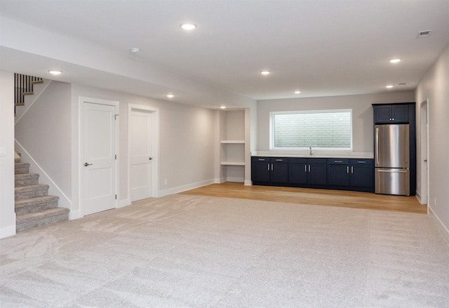 unfurnished living room with light carpet, built in shelves, and sink