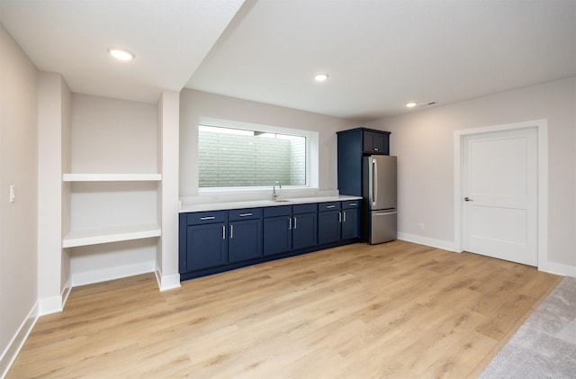 kitchen with light hardwood / wood-style floors, blue cabinets, sink, and stainless steel refrigerator