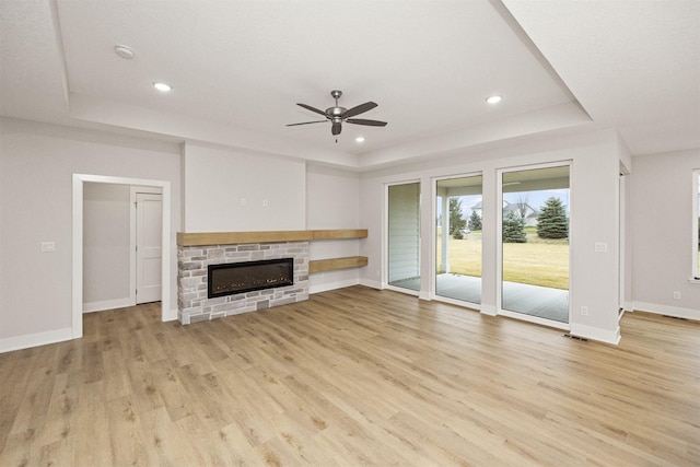 unfurnished living room featuring ceiling fan, light hardwood / wood-style floors, a stone fireplace, and a tray ceiling