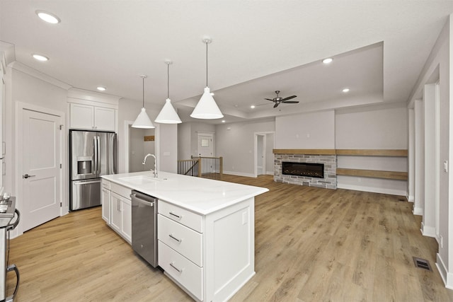 kitchen featuring stainless steel appliances, ceiling fan, a center island with sink, white cabinets, and hanging light fixtures