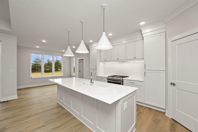 kitchen with backsplash, stainless steel gas range oven, sink, decorative light fixtures, and an island with sink