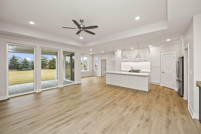 unfurnished living room featuring a tray ceiling, ceiling fan, and light hardwood / wood-style flooring