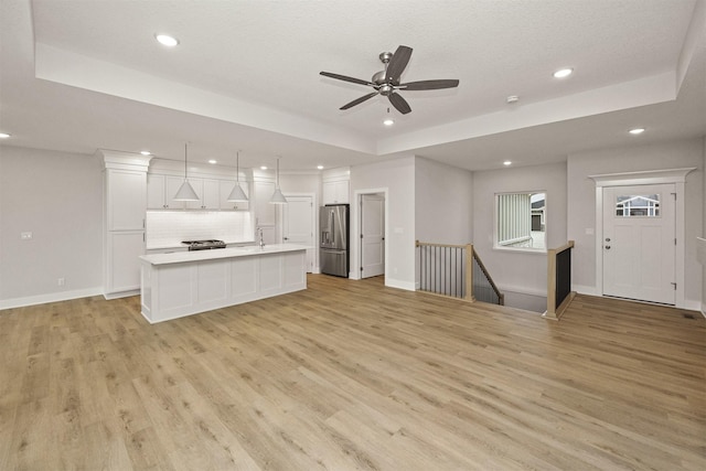 unfurnished living room featuring light hardwood / wood-style flooring, a raised ceiling, ceiling fan, and sink