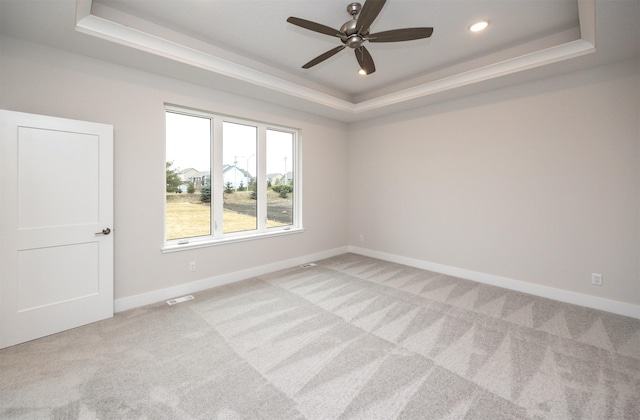 unfurnished room featuring a tray ceiling, light carpet, and ceiling fan