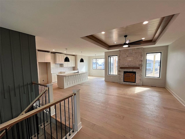 unfurnished living room with a fireplace, plenty of natural light, light hardwood / wood-style floors, and a raised ceiling