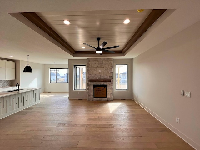 unfurnished living room with a stone fireplace, sink, a tray ceiling, wooden ceiling, and light hardwood / wood-style flooring