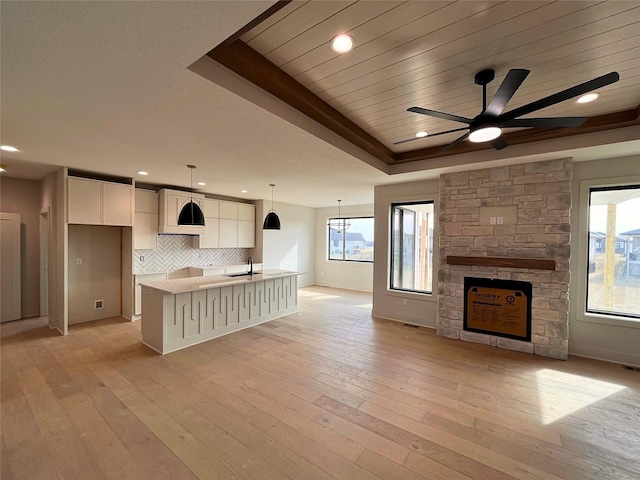 kitchen with a stone fireplace, white cabinetry, hanging light fixtures, light hardwood / wood-style flooring, and a raised ceiling