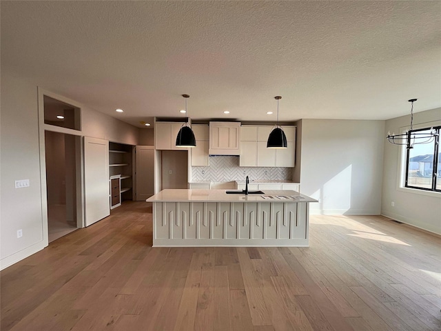 kitchen with an island with sink, sink, pendant lighting, and light hardwood / wood-style flooring