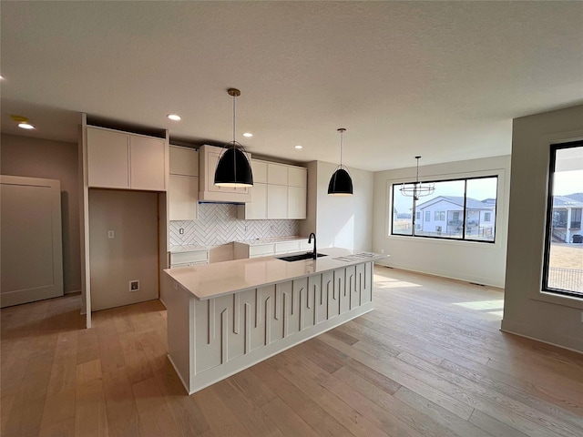 kitchen with pendant lighting, white cabinetry, sink, a center island with sink, and light wood-type flooring