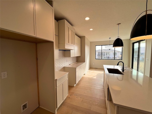 kitchen featuring sink, light hardwood / wood-style flooring, white cabinets, pendant lighting, and backsplash