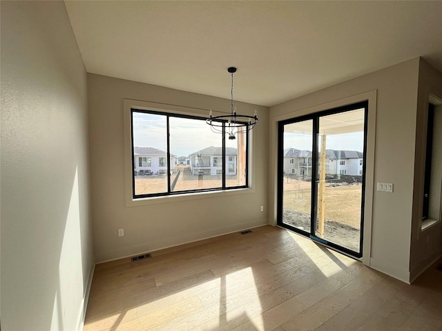 unfurnished dining area with an inviting chandelier and light hardwood / wood-style floors