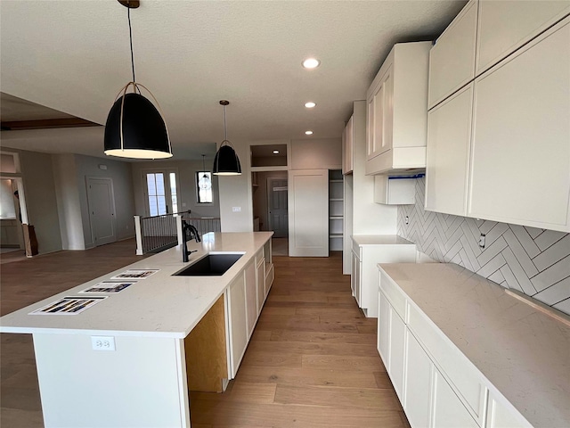 kitchen featuring sink, white cabinetry, hanging light fixtures, a center island with sink, and light wood-type flooring