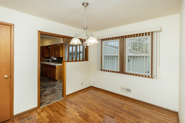 unfurnished dining area with sink, hardwood / wood-style floors, and a notable chandelier