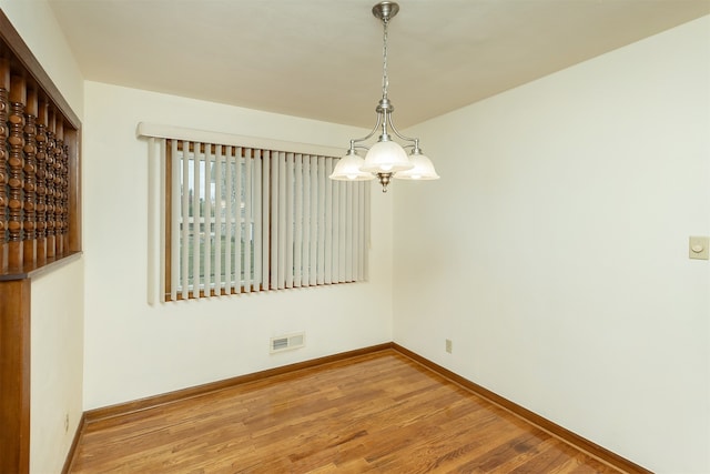 spare room featuring wood-type flooring and an inviting chandelier