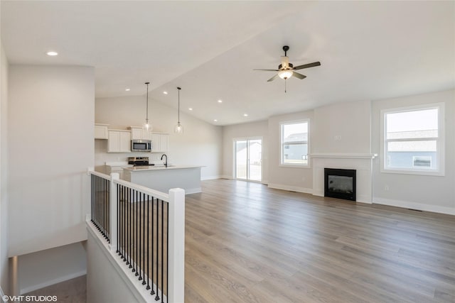 kitchen featuring appliances with stainless steel finishes, decorative light fixtures, light hardwood / wood-style flooring, white cabinets, and lofted ceiling