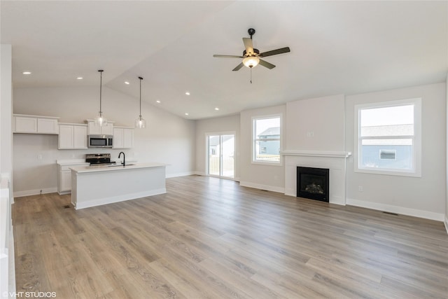 unfurnished living room featuring light hardwood / wood-style floors, ceiling fan, lofted ceiling, and sink