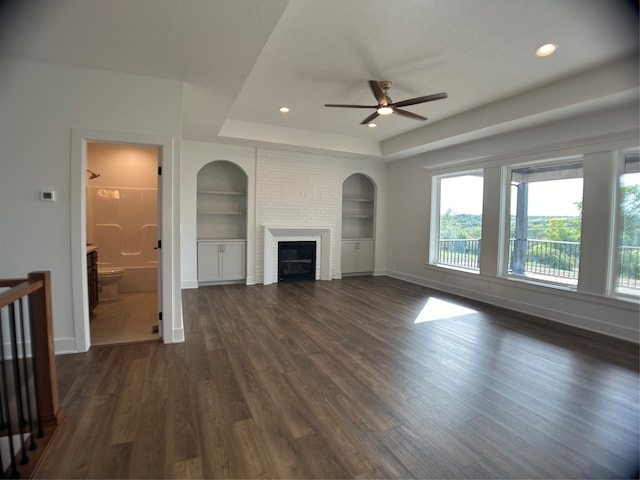 unfurnished living room with dark hardwood / wood-style flooring, ceiling fan, a raised ceiling, a fireplace, and built in shelves