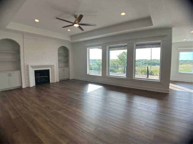 unfurnished living room featuring dark hardwood / wood-style floors, ceiling fan, a fireplace, and built in shelves