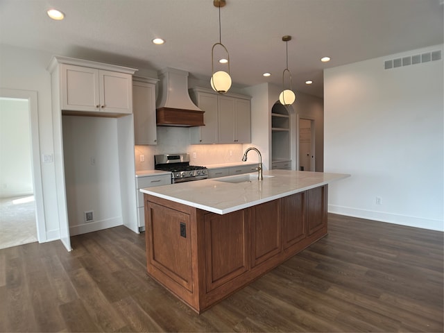 kitchen with hanging light fixtures, an island with sink, custom range hood, stainless steel range with gas cooktop, and sink