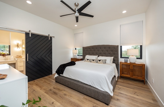 bedroom with ceiling fan, light wood-type flooring, and a barn door