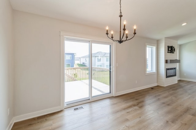 unfurnished dining area with a notable chandelier, a large fireplace, and light wood-type flooring