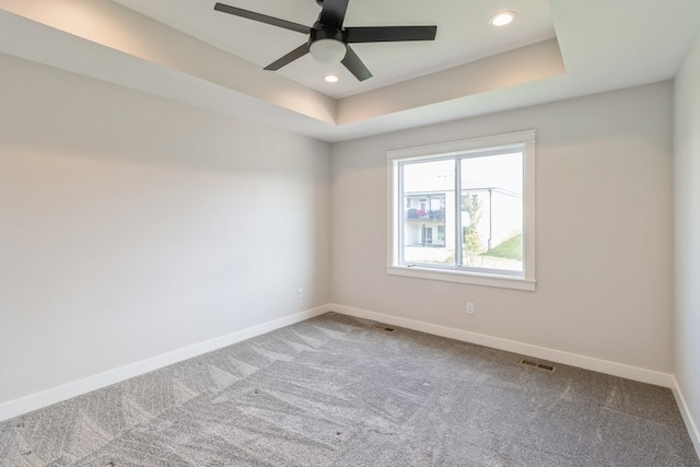 empty room with carpet, a tray ceiling, and ceiling fan