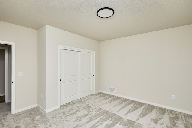 unfurnished bedroom featuring a textured ceiling, a closet, and light carpet