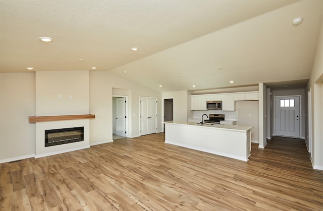 unfurnished living room featuring sink, vaulted ceiling, and light hardwood / wood-style floors