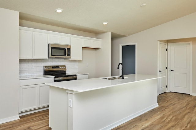 kitchen featuring stainless steel appliances, white cabinetry, a center island with sink, and backsplash