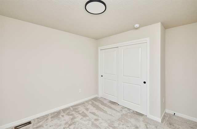 unfurnished bedroom with light colored carpet, a textured ceiling, and a closet