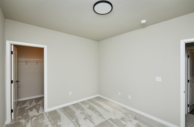 unfurnished bedroom with light carpet, a textured ceiling, a closet, and a spacious closet