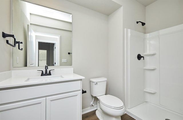 bathroom with hardwood / wood-style flooring, toilet, walk in shower, and vanity